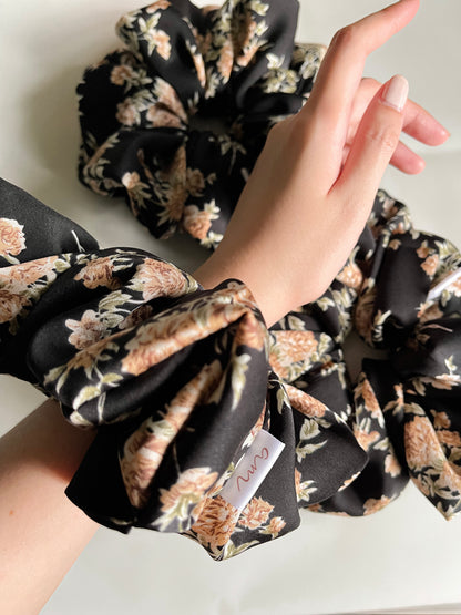 A picture of 3 black floral oversized scrunchie. One is worn on the wrist.